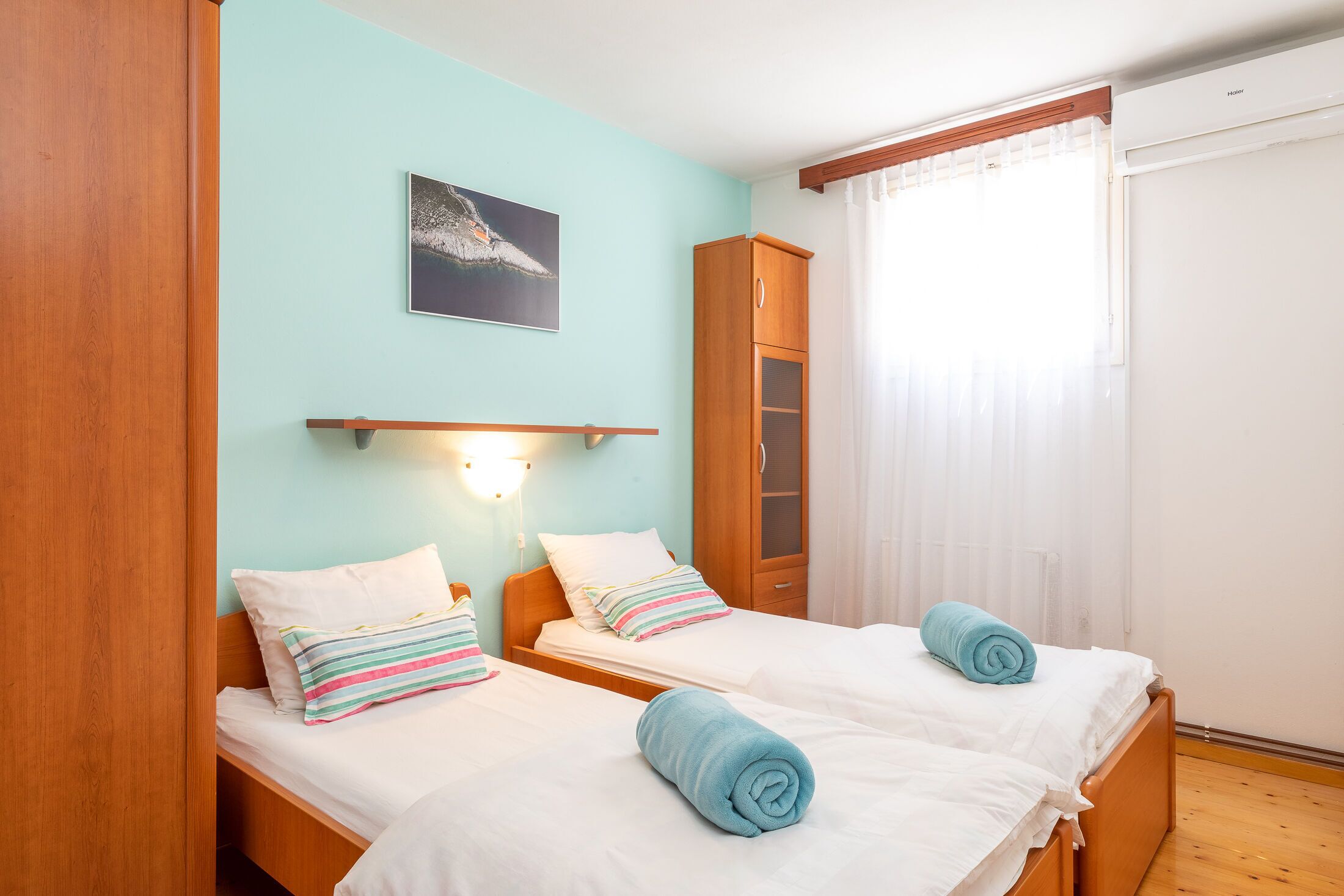 Ein Hotelzimmer mit zwei Betten, einem Holzschrank, einer Wandablage und einem Fenster mit Vorhängen.