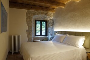 Un dormitorio con pared de piedra, una ventana, un radiador y una cama con ropa de cama blanca.