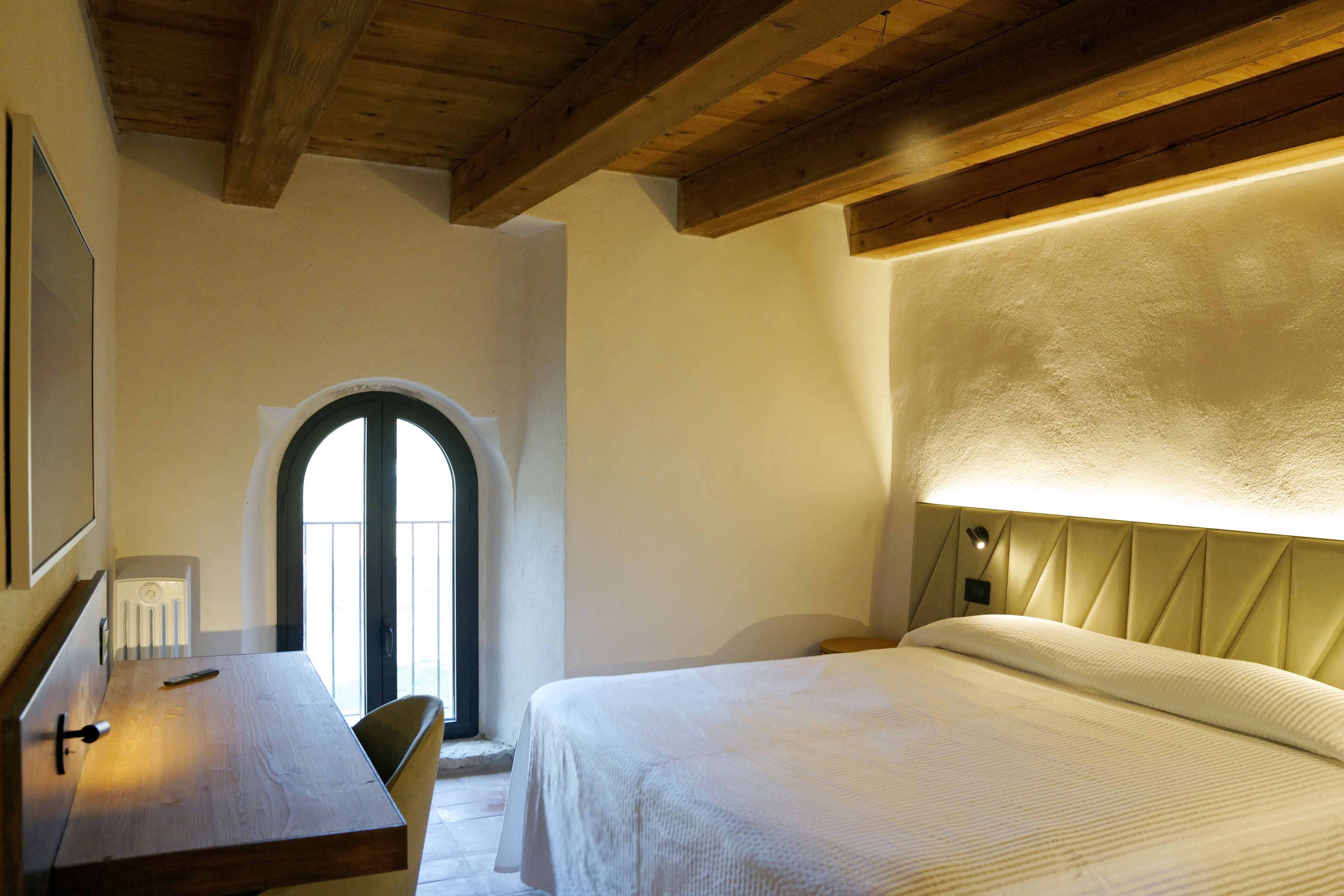 A bedroom with a wooden ceiling, a bed with a headboard, a desk, and a chair.