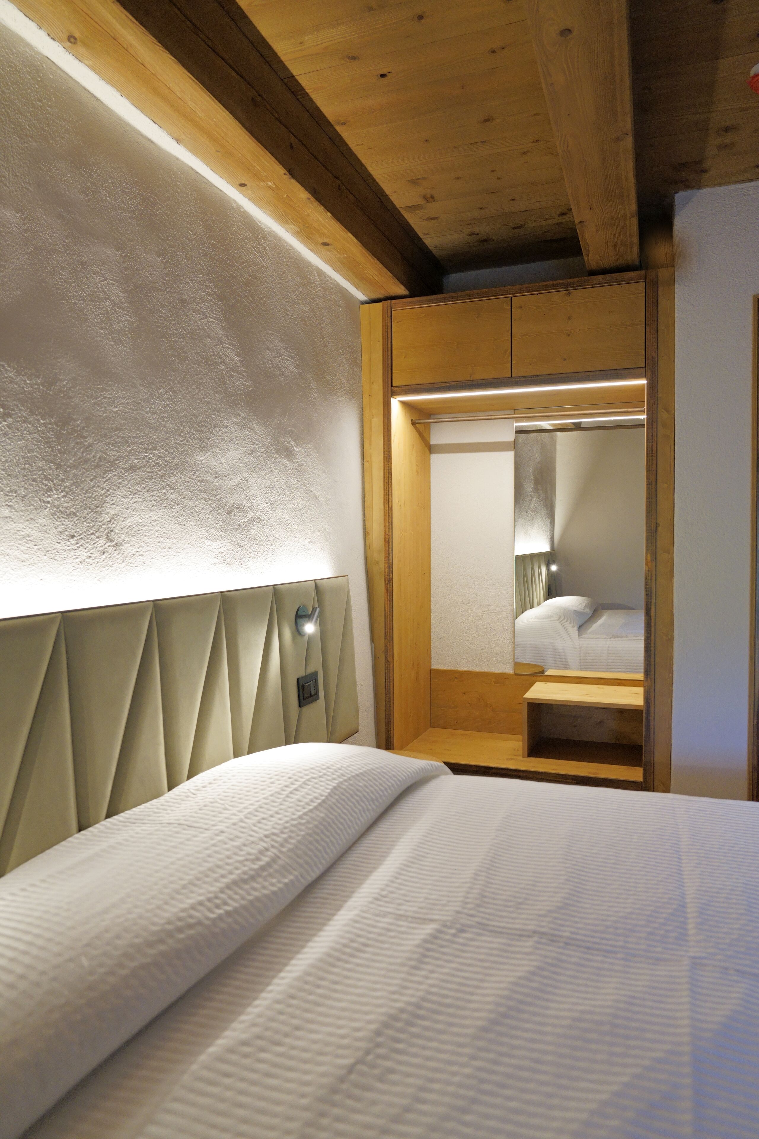A bedroom with a bed, a headboard, a mirror, and a bedside table.