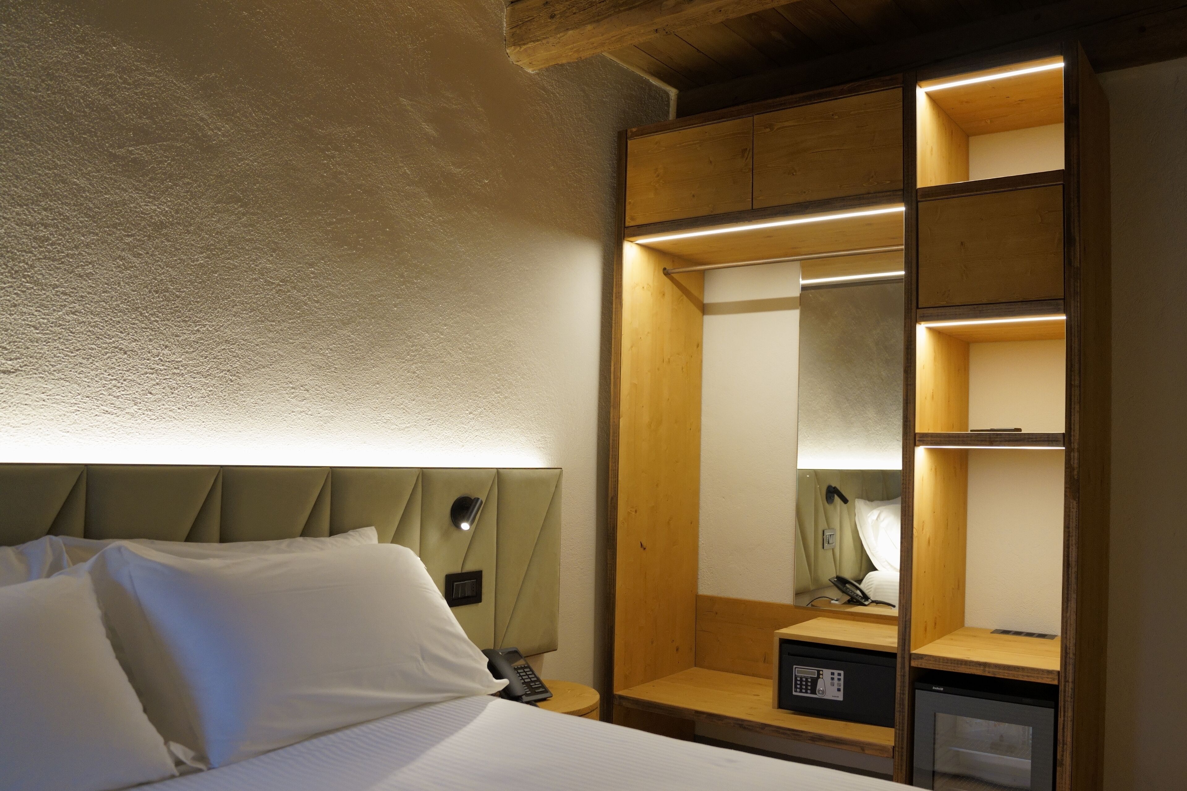 Una camera d'albergo con un letto, un comodino, una lampada e un'armadio in legno con ripiani.