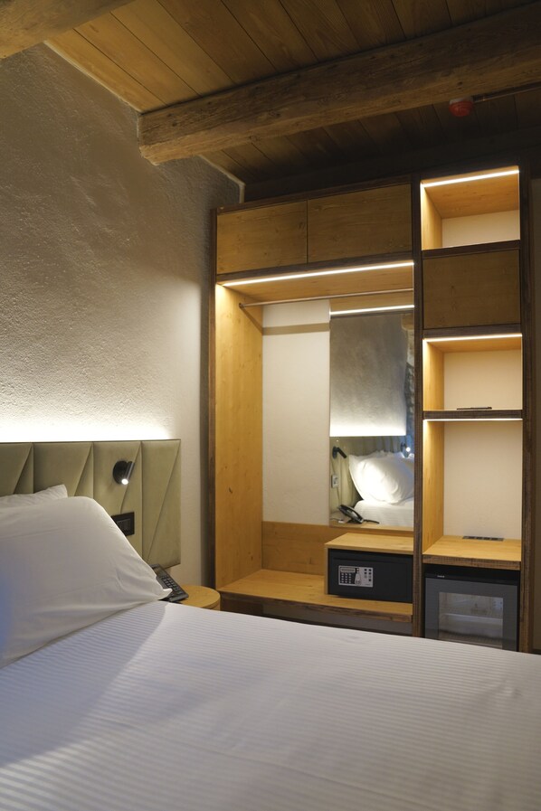 A hotel room with a bed, a bedside table with a lamp, a built-in wardrobe, and a small refrigerator. - Monastero Sant Alberico Relais (Verghereto)
