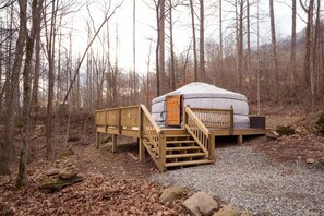 Experience the tranquility of a traditional yurt, nestled in a forested area, with a wooden staircase leading to its entrance.