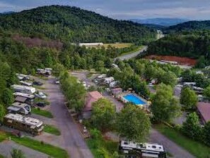 Escape to a serene valley setting with RVs and trailers nestled among lush greenery and a nearby swimming pool.