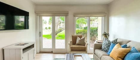 A living room with a sofa, coffee table, TV, and a sliding glass door leading to a garden.