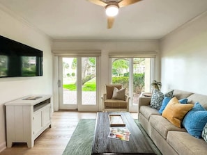A living room with a sofa, coffee table, TV, and a sliding glass door leading to a garden.