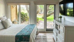 Un dormitorio con cama, televisión, cómoda y puerta corrediza de vidrio que da a un patio.