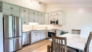 Una cocina moderna con electrodomésticos de acero inoxidable, armarios blancos y una mesa de comedor de mármol.