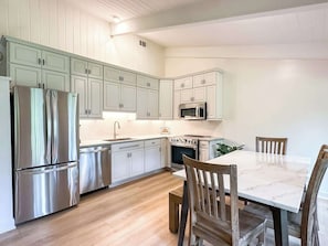 A modern kitchen with stainless steel appliances, white cabinetry, and a marble dining table.