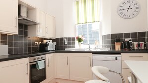 A modern kitchen with white cabinets, a black countertop, and a wooden floor. - Spinners House (Dartmouth)