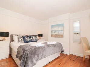 Ein Schlafzimmer mit einem Bett, zwei Nachttischlampen, einem Meeresbild, einem Sessel und einem Holzboden.