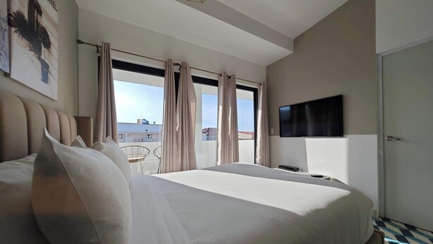 Ein Hotelzimmer mit einem großen Bett, einem an der Wand montierten Fernseher, einem Fenster mit Vorhängen und Blick auf die Stadtlandschaft.