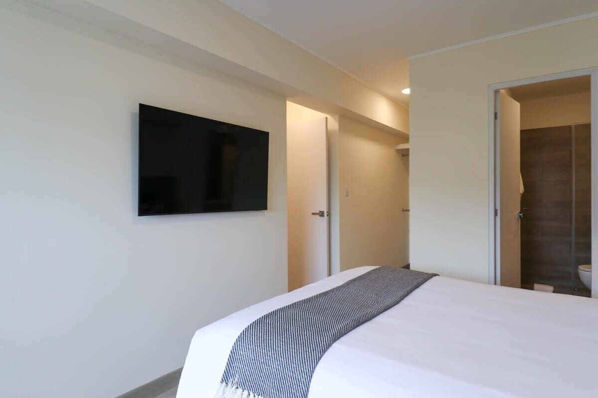 Een hotelkamer met een bed, een flatscreen televisie aan de wand en een douchecel zichtbaar door een geopende deur.