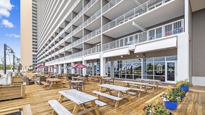 Eine Dachterrasse mit Holztischen und -stühlen, Pflanzgefäßen und Blick auf ein Gebäude mit Balkonen.