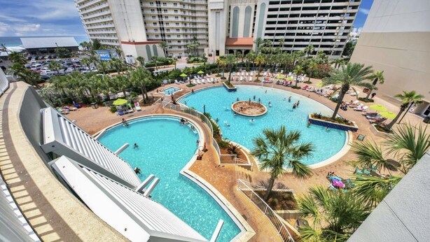 Ein Resort mit mehreren Schwimmbecken, Palmen und einem Parkplatz.