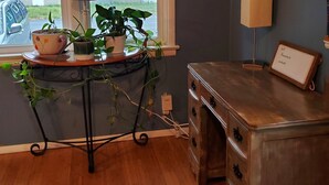 Una habitación con un escritorio de madera, una planta sobre una mesa, un reloj en la pared y una ventana con persianas.