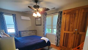 Un dormitorio con cama, cómoda, ventilador de techo, ventana con cortinas y puerta.
