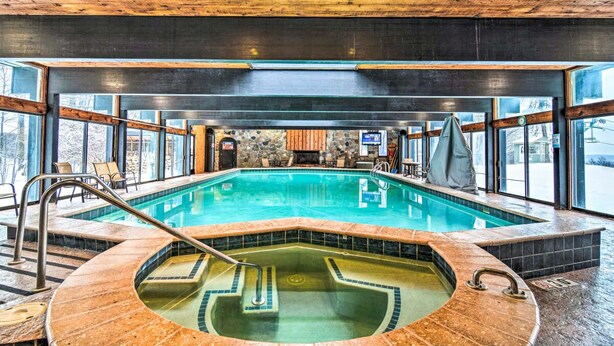 Ein großes Hallenbad mit separatem Whirlpoolbereich, umgeben von großen Fenstern und einer Steinwand.