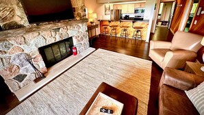 Ein Wohnzimmer mit Kamin aus Stein, einem Flachbildfernseher, einem Ledersofa und einer Bar mit Sitzhocker.