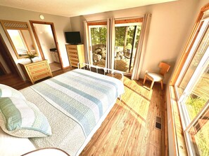 A bedroom with a large bed, wooden flooring, a dresser, a television, and a window with curtains.
