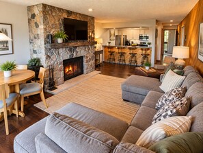 A modern living room with a stone fireplace, a dining area, and a kitchen in the background. - Very Private Updated 2Br Condo on the Summit. Walking distance to all the fun. (Bellaire)