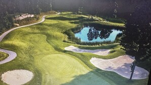 Ein Golfplatz mit Teich, Sandbunkern und einem Fußweg.