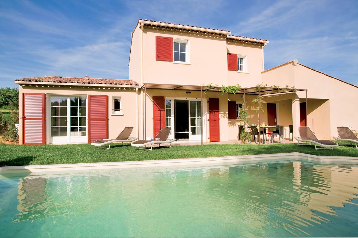 A two-story house with a swimming pool, red shutters, and a patio with outdoor furniture.