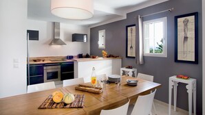 A modern kitchen with a dining area, featuring a wooden table, white chairs, and a hanging light fixture.