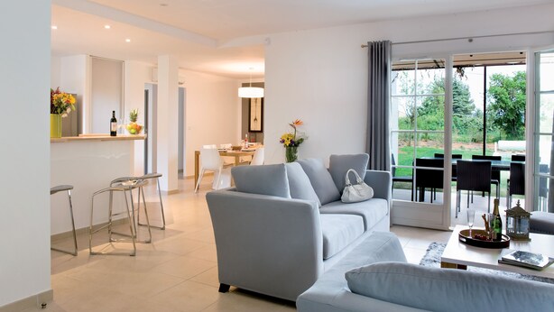 A modern living room with a grey sofa, a coffee table, and a dining area with a table and chairs.