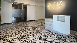 Un hall d’hôtel moderne avec un sol à motifs géométriques, un comptoir d’accueil et une enseigne fixée au mur indiquant « Hôtel Z-TRIHOA ».