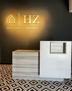 A reception desk with a geometric patterned floor, a wall-mounted sign for HOTEL Z-TRILOA, and a modern, minimalist design. - U by Z Hotels Bellandur (Bengaluru)