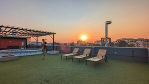Une terrasse sur le toit offrant une vue sur le coucher de soleil, avec des chaises longues et une structure en forme de pergola.
