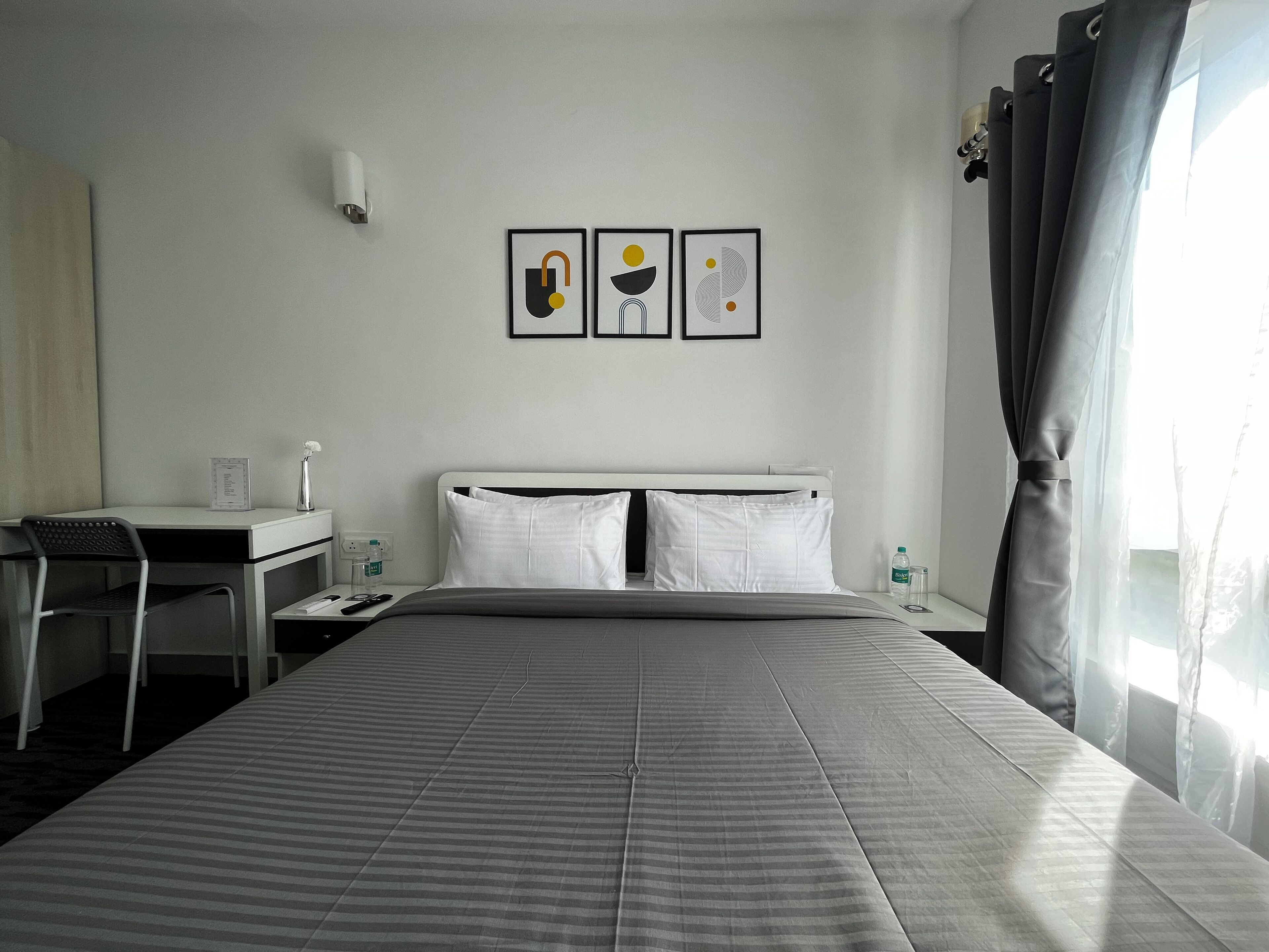 Una camera d'albergo con un letto, una scrivania e una sedia. In parete, tre quadri incorniciati.