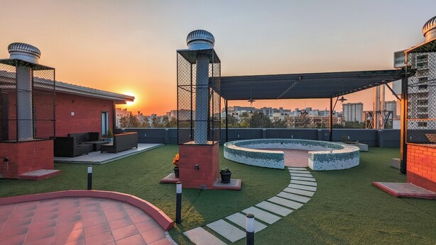 Une terrasse sur le toit avec un espace salon circulaire, un mur en briques et une vue sur les toits de la ville au coucher du soleil.