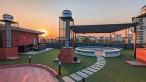 Une terrasse sur le toit avec un espace salon circulaire, un mur en briques et une vue sur les toits de la ville au coucher du soleil.