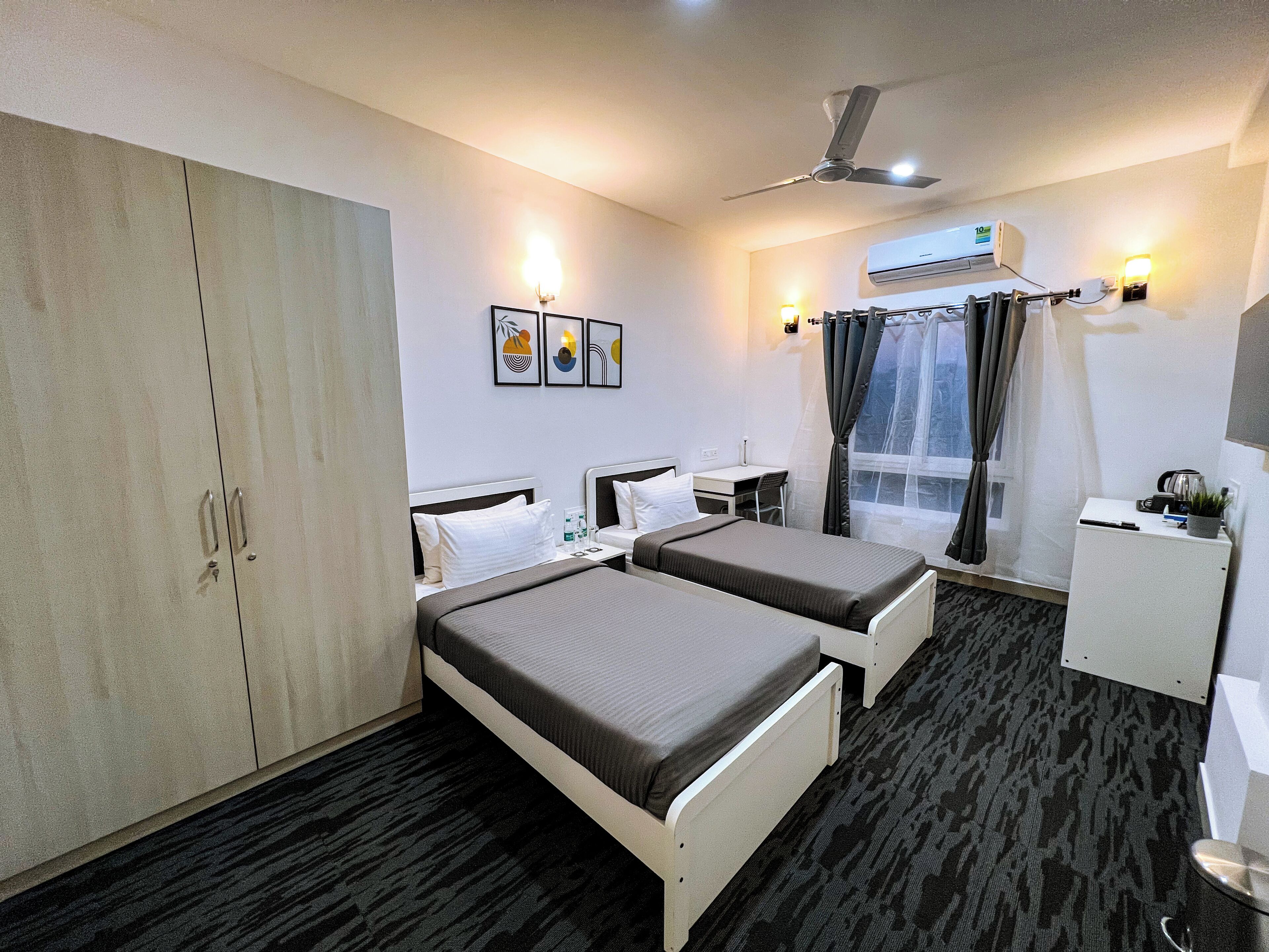 Een hotelkamer met twee eenpersoonsbedden, een garderobe, een bureau, een stoel, een klein kastje en een raam met gordijnen.