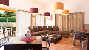 A modern living room with a sectional sofa, a glass coffee table, and a dining area with a table and chairs. There are pendant lights above the sofa and dining table. - Lagrange Vacances - Green Bastide (Roquebrune-sur-Argens)