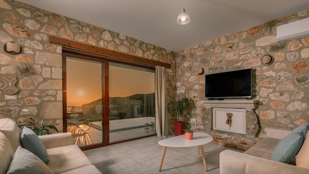 A cozy living room with stone walls, a flat-screen TV, a fireplace, and comfortable seating. - Arca Villa - Enchanting Sunset! (Zakynthos)
