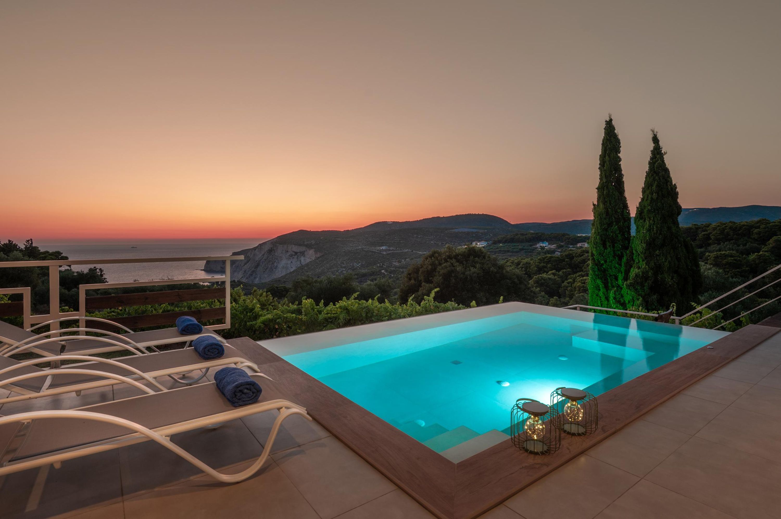Una piscina infinita en la azotea con sillones de descanso y vista al atardecer sobre el mar.