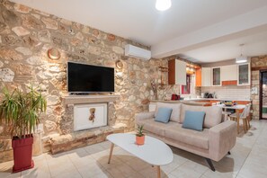 A living room with a stone wall, a flat-screen TV, a sofa, a coffee table, and a potted plant.