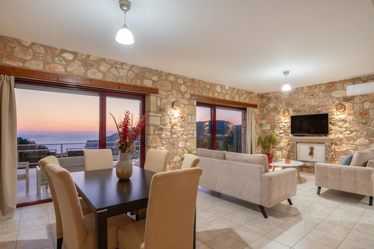 A spacious living area with a stone wall, a flat-screen TV, and a dining table with chairs.