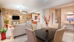 A modern living room with a stone wall, a flat-screen TV, a sofa, and a dining table with chairs. - Arca Villa - Enchanting Sunset! (Zakynthos)