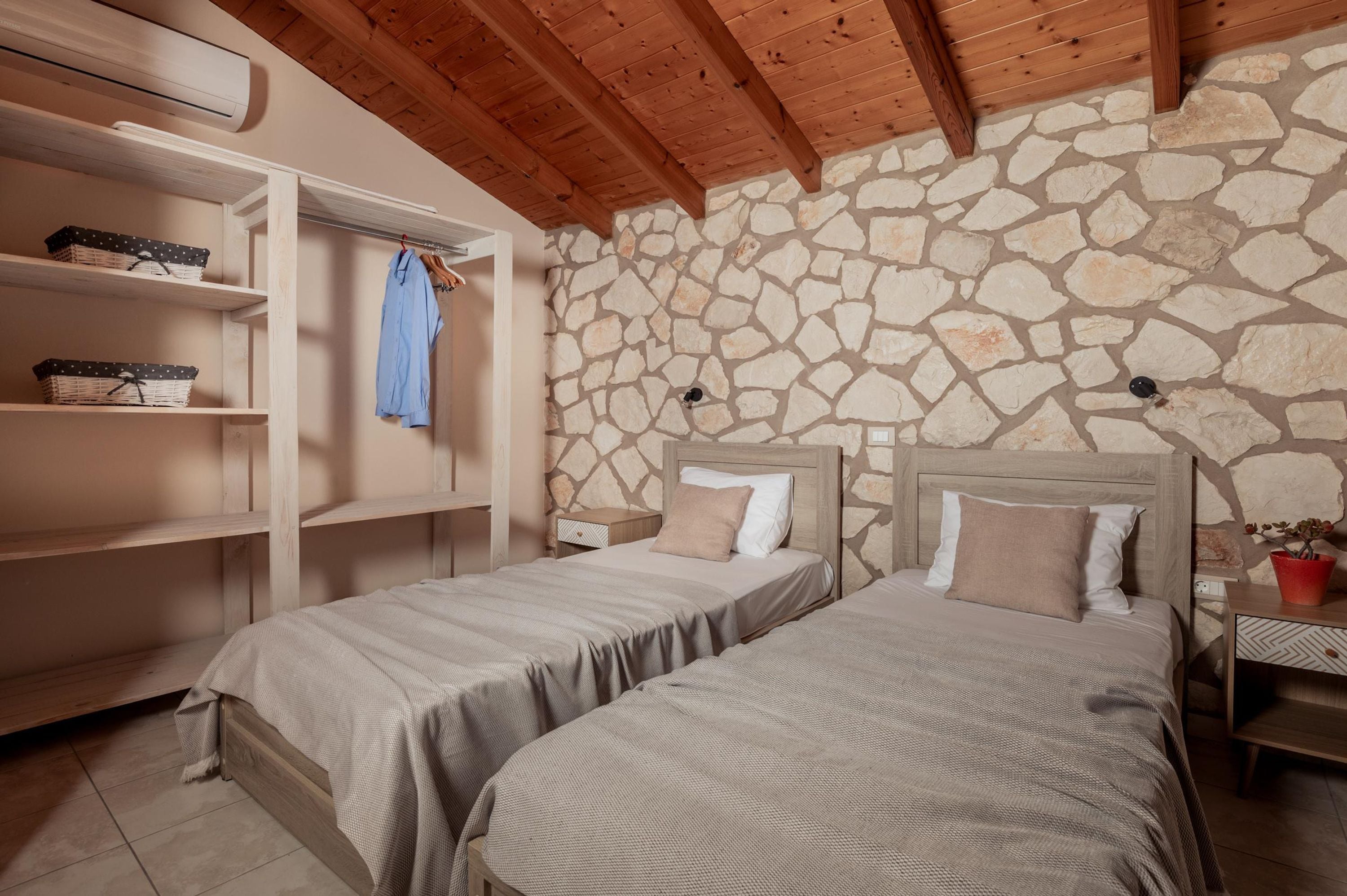 A bedroom with two beds, wooden headboards, a stone wall, and a wooden ceiling.