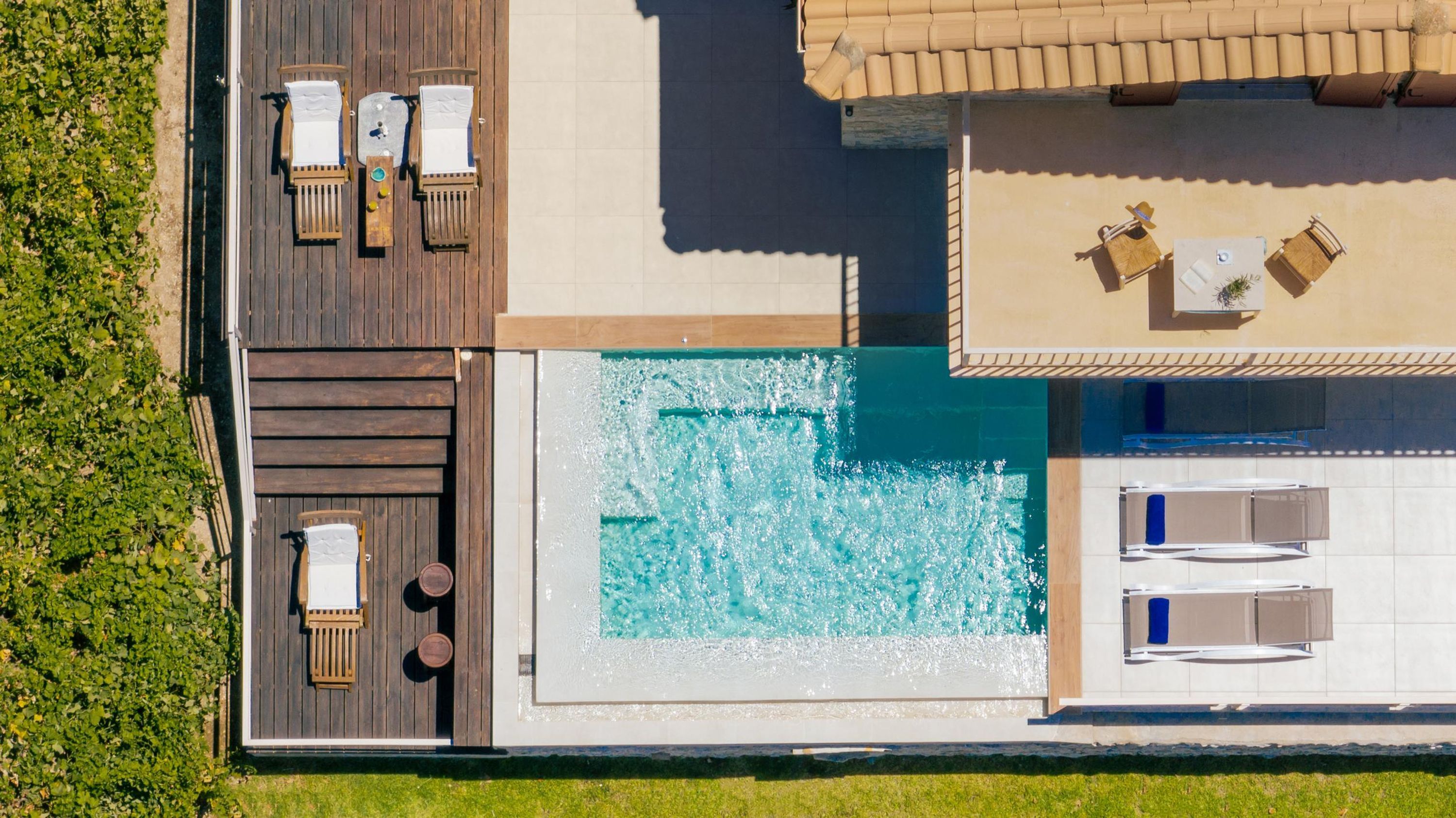 An aerial view of a resort with a swimming pool, wooden deck, and lounge chairs.