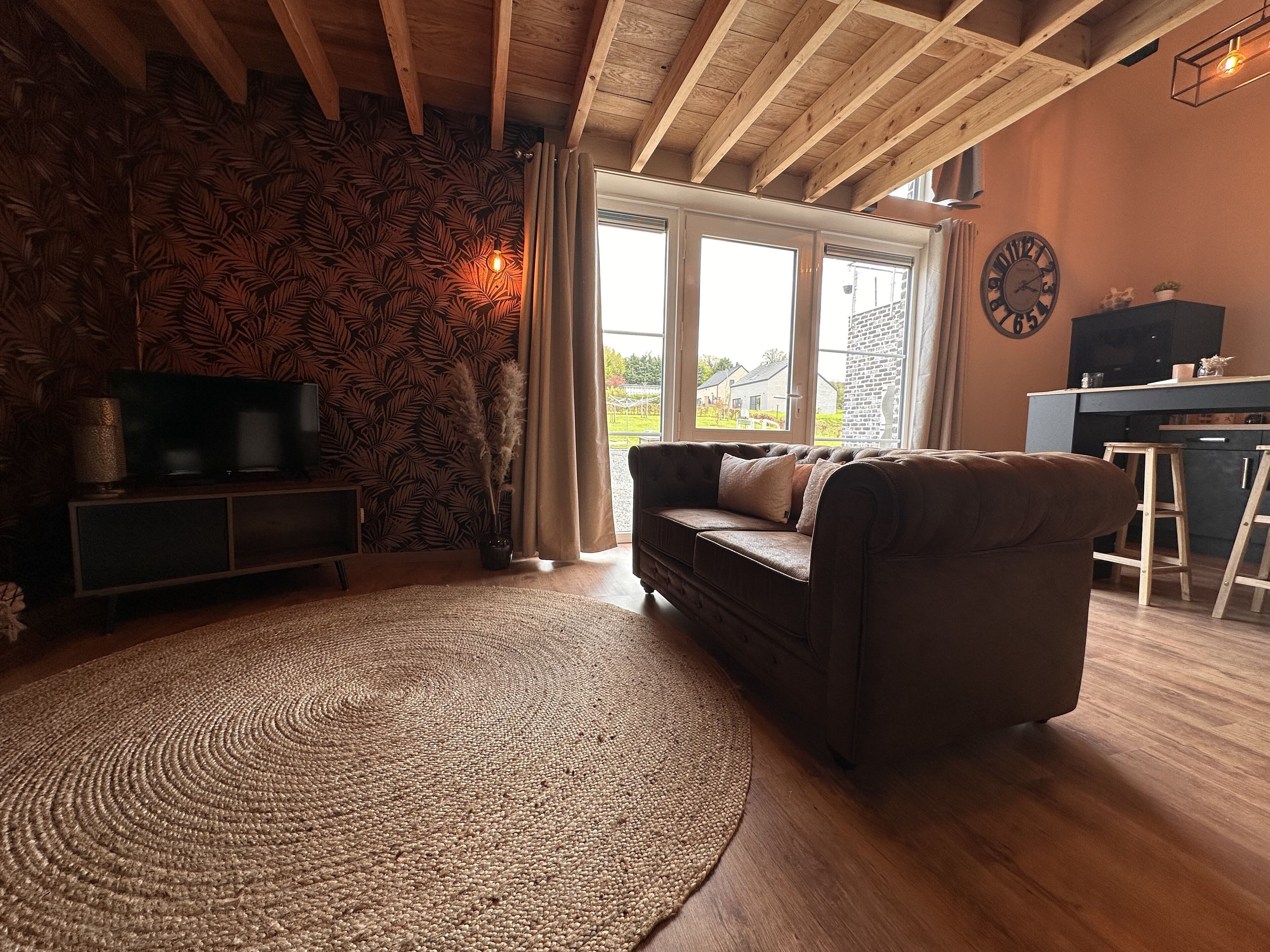 Un salon chaleureux avec un canapé marron, un tapis tissé et un plafond en bois.
