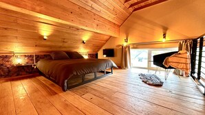 Un dormitorio acogedor con techo de madera, una cama, una silla y una ventana con cortinas.