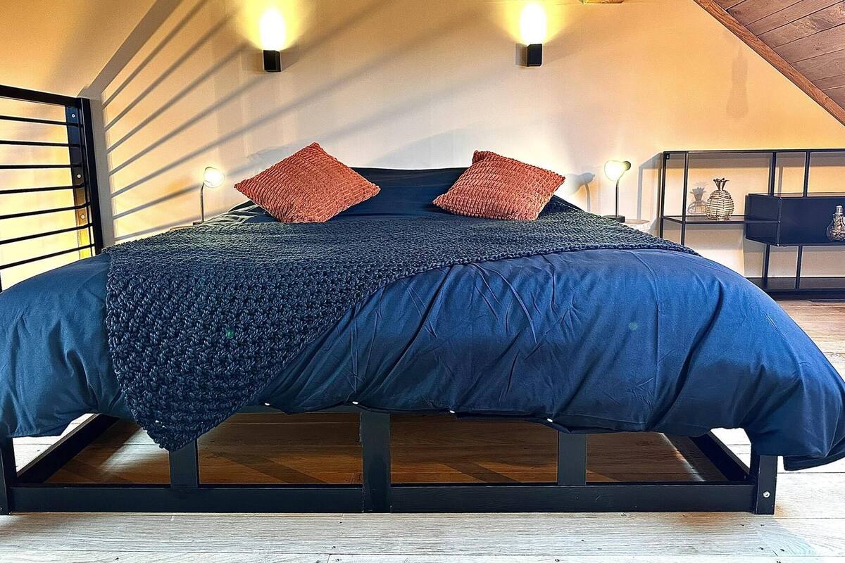 Quarto com cama, duas luzes fixadas na parede e teto de madeira.