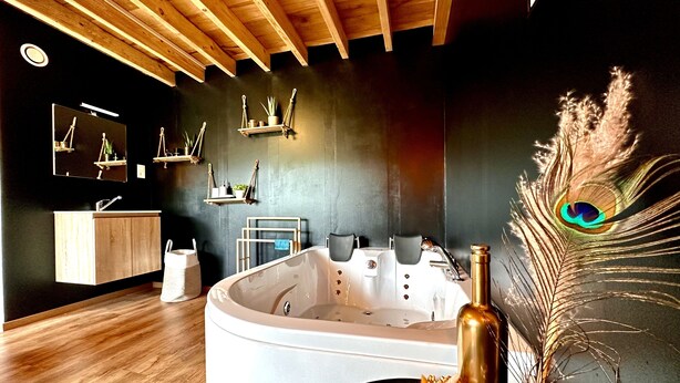 Un baño moderno con una bañera independiente, vigas de techo de madera, un tocador con espejo y estantes decorativos en la pared.