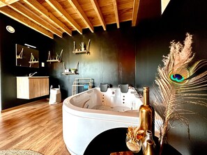 Un baño moderno con una bañera independiente, vigas de techo de madera, un tocador con espejo y estantes decorativos en la pared.