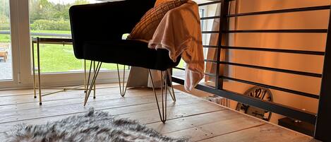 Une pièce avec une grande fenêtre, une chaise noire, un chien à la fourrure douce et un porte-serviettes en métal avec une serviette.